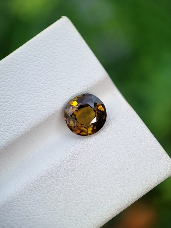 A photo of a loose faceted Epidote gemstone with a greenish-orange color and oval shape from Pakistan | 1.99 ct