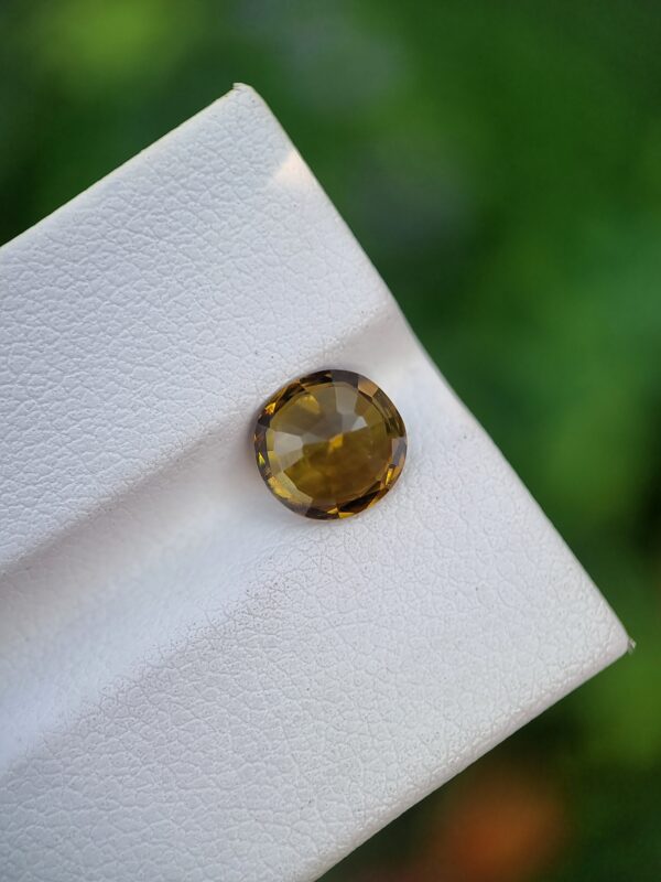 A photo of a loose faceted Epidote gemstone with a greenish-orange color and oval shape from Pakistan | 1.99 ct