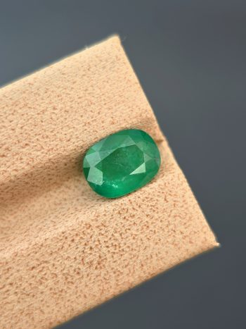 A professionally lit, detailed photograph of a 2.03 ct natural green emerald from the Swat Valley, Pakistan, in an oval cut. The stone is transparent with visible inclusions.
