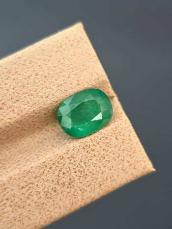 A professionally lit, detailed photograph of a 2.03 ct natural green emerald from the Swat Valley, Pakistan, in an oval cut. The stone is transparent with visible inclusions.