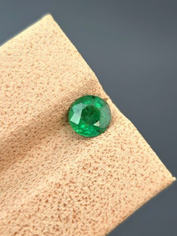 A detailed photograph of a 0.68 ct natural emerald from the Swat Valley, Pakistan. The stone is a rare round cut with a green color and visible internal inclusions.
