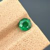 A detailed photograph of a 0.68 ct natural emerald from the Swat Valley, Pakistan. The stone is a rare round cut with a green color and visible internal inclusions.
