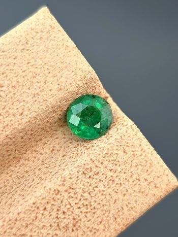 A detailed photograph of a 0.68 ct natural emerald from the Swat Valley, Pakistan. The stone is a rare round cut with a green color and visible internal inclusions.