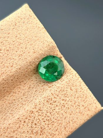 A detailed photograph of a 0.68 ct natural emerald from the Swat Valley, Pakistan. The stone is a rare round cut with a green color and visible internal inclusions.
