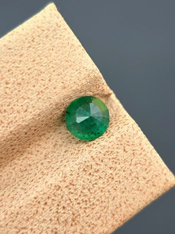A detailed photograph of a 0.68 ct natural emerald from the Swat Valley, Pakistan. The stone is a rare round cut with a green color and visible internal inclusions.