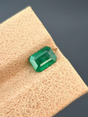A clear photograph of a 0.94 carat natural emerald with an emerald cut and green color. The stone is from the Swat Valley and has visible internal inclusions.
