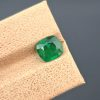A high-resolution, well-lit image of a 1.60 carat natural green emerald from Pakistan. The stone is a cushion cut with visible internal inclusions.