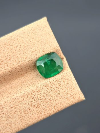 A high-resolution, well-lit image of a 1.60 carat natural green emerald from Pakistan. The stone is a cushion cut with visible internal inclusions.