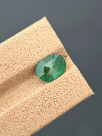 A well-lit, professional image of a 1.68 carat natural emerald from the Swat Valley, Pakistan. The gemstone has an oval cut, a green color, and visible inclusions.