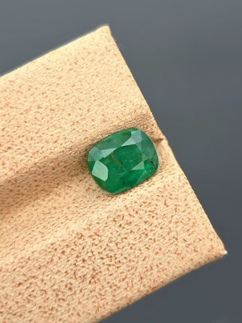 A clear, close-up photograph of a 1.18 carat natural emerald from Pakistan's Swat Valley. The stone is a cushion cut with a green color and visible internal inclusions.