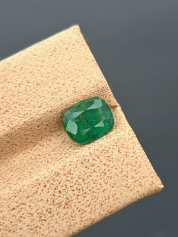 A clear, close-up photograph of a 1.18 carat natural emerald from Pakistan's Swat Valley. The stone is a cushion cut with a green color and visible internal inclusions.