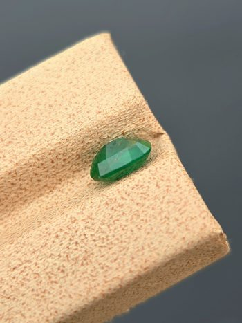 A clear, close-up photograph of a 1.18 carat natural emerald from Pakistan's Swat Valley. The stone is a cushion cut with a green color and visible internal inclusions.