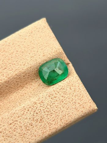 A clear, close-up photograph of a 1.18 carat natural emerald from Pakistan's Swat Valley. The stone is a cushion cut with a green color and visible internal inclusions.
