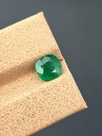 A high-quality image of a 1.09 carat natural cushion-cut green emerald with visible inclusions, photographed against a neutral background. The gemstone is from the Swat Valley in Pakistan.